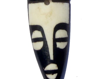 May include: Black and white carved wooden pendant in the shape of a face. The face has a crown on top and simple features.