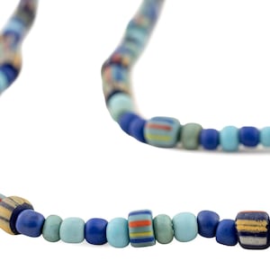 May include: A necklace featuring a variety of blue, green, and tan beads. The beads are cylindrical and round, with some displaying striped patterns in orange, yellow, and blue. The necklace is strung on a flexible cord.