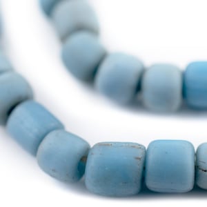 Op de afbeelding: Close-up van een streng lichtblauwe, vierkante kralen. De kralen hebben een licht verweerde uitstraling, met variaties in de blauwe tint. De kralen zijn aan elkaar geregen, waardoor een ketting of armband ontstaat.