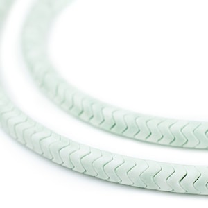 Puede incluir: Primer plano de un collar flexible de color verde claro con un patrón en zigzag. El collar está hecho de una serie de piezas conectadas entre sí.