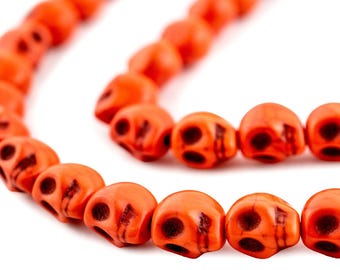 May include: Close-up of a strand of orange skull beads. The beads are a vibrant orange color with dark accents, and each bead is shaped like a skull. The beads are strung together, creating a curved line against a white background.