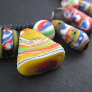 May include: A colorful glass bead necklace with a variety of patterns and colors, including yellow, red, blue, green, and black.