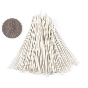 May include: A pile of silver-toned head pins, approximately 1 inch long, with a flat head. The pins are arranged in a fan shape and are next to a US penny for scale.