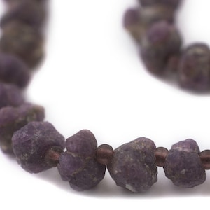 May include: A close-up of a purple gemstone necklace. The necklace is made of small, irregular shaped stones that are strung together with brown thread.