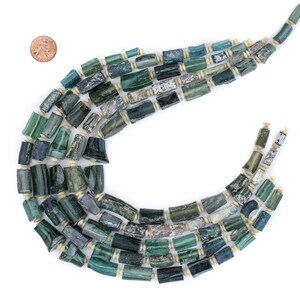 May include: A strand of green and blue glass beads with white spacers. The beads are cylindrical and have a slightly irregular shape. The beads are strung on a cord and are arranged in a loose, flowing pattern.