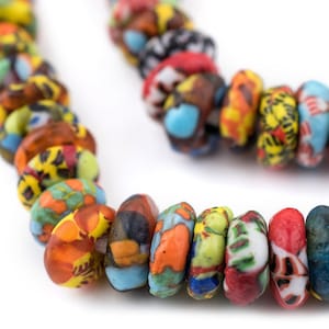May include: A close-up shot of a vibrant necklace composed of patterned, oblong beads. The beads showcase a mix of colours such as red, yellow, blue, and orange, with detailed designs. The necklace is set against a white backdrop.