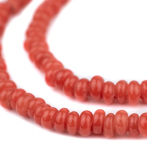 Könnte beinhalten: Eine Kette aus roten Korallenperlen, die zu einer Halskette zusammengefügt sind. Die Perlen sind rund und glatt, mit einer glänzenden Oberfläche.