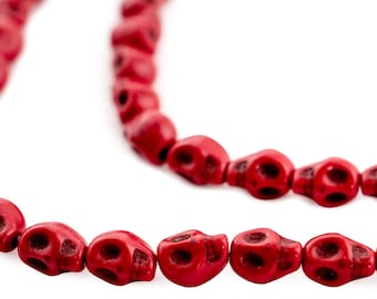 May include: Close-up of a necklace made of red skull beads. The beads are strung together, forming a curved line against a white background. The skulls have detailed features and a glossy finish.