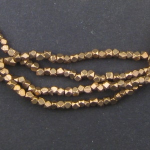 May include: A strand of gold-toned metal beads. Each bead is faceted and has a geometric shape.