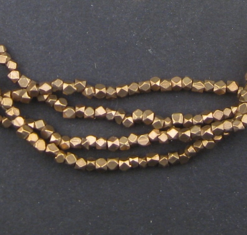 May include: A strand of gold-toned metal beads. Each bead is faceted and has a geometric shape.
