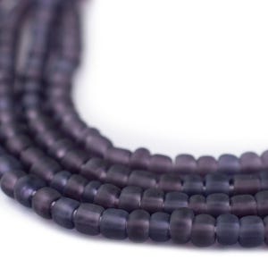 May include: Close-up of strands of dark purple beads. The beads are small, cylindrical, and have a matte finish. The beads are arranged in multiple strands, creating a layered effect. The background is plain white, highlighting the beads.
