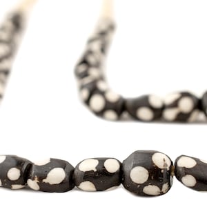 May include: A close-up of a necklace with dark brown beads featuring white polka dots. The beads are irregularly shaped and strung together. The necklace is set against a white background.