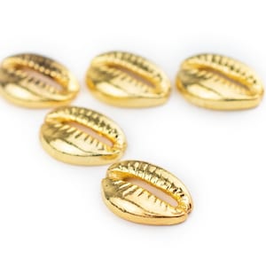 May include: Five gold cowrie shells, a type of seashell, are arranged in a row on a white background.