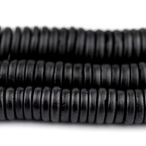 Puede incluir: Primer plano de cuentas de madera negras, apiladas en filas. Las cuentas son redondas y tienen un acabado liso y pulido.