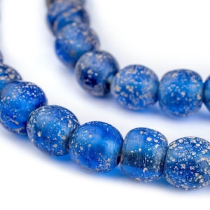 Pode incluir: Close-up de duas fileiras de contas redondas azuis com uma aparência salpicada e envelhecida. As contas são de um azul profundo e saturado com salpicos brancos e azul claro, criando uma textura única. As contas são enfiadas, sugerindo joias.