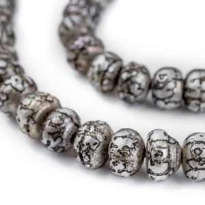 Könnte beinhalten: Eine Kette aus silberfarbenen Perlen mit komplizierten Mustern. Die Perlen sind rund und haben eine leicht strukturierte Oberfläche.