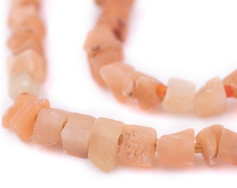 May include: A close-up of a strand of light orange and peach colored gemstone beads. The beads are irregularly shaped and have a rough, natural texture.