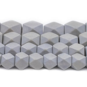 Puede incluir: Primer plano de una fila de cuentas de piedra gris. Las cuentas son facetadas y tienen una superficie ligeramente texturizada.