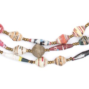 May include: A multi-strand necklace made of colorful paper beads. The beads are made from rolled up pieces of paper and have a variety of patterns and colors. The necklace is strung on a gold-colored cord.