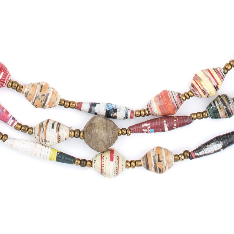 May include: A multi-strand necklace made of colorful paper beads. The beads are made from rolled up pieces of paper and have a variety of patterns and colors. The necklace is strung on a gold-colored cord.