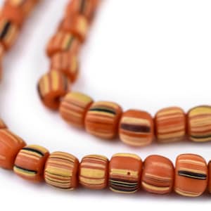 May include: Close-up of a strand of orange barrel-shaped beads. Each bead features horizontal stripes in shades of yellow, brown, and black. The beads are strung together, creating a necklace or bracelet.
