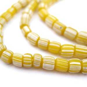 May include: A strand of yellow and white striped glass beads. The beads are cylindrical and have a glossy finish.