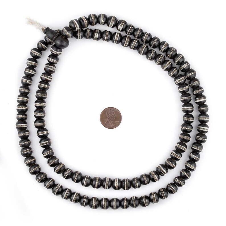 May include: A black and white beaded necklace with a tassel. The beads are round and have a white stripe around the middle. The necklace is about 18 inches long.