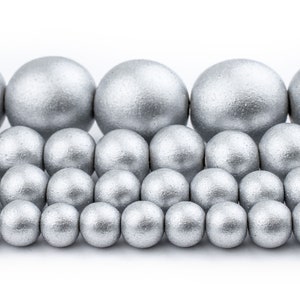 May include: A collection of silver-colored round beads of varying sizes. The beads are arranged in a staggered pattern, creating a visual effect of a wave.