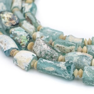 May include: A close-up of a necklace made of light blue and white glass beads. The beads are irregular in shape and have a worn, antique look.