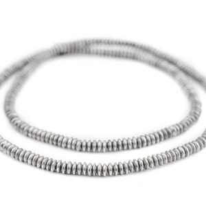 K&ouml;nnte beinhalten: Eine silberfarbene Halskette aus kleinen, gleichm&auml;&szlig;ig verteilten, scheibenf&ouml;rmigen Perlen. Die Kette wird vor einem wei&szlig;en Hintergrund pr&auml;sentiert, der ihren metallischen Glanz und ihr schlichtes Design hervorhebt. Die Perlen scheinen gleichm&auml;&szlig;ig gro&szlig; zu sein.