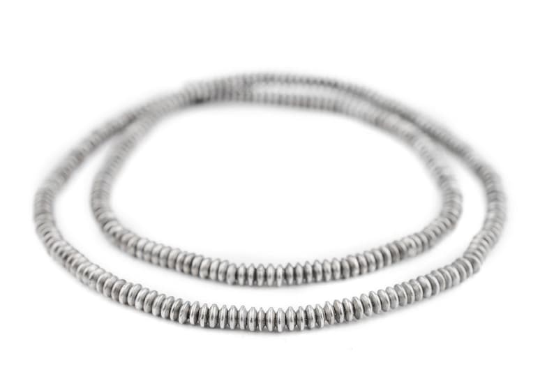K&ouml;nnte beinhalten: Eine silberfarbene Halskette aus kleinen, gleichm&auml;&szlig;ig verteilten, scheibenf&ouml;rmigen Perlen. Die Kette wird vor einem wei&szlig;en Hintergrund pr&auml;sentiert, der ihren metallischen Glanz und ihr schlichtes Design hervorhebt. Die Perlen scheinen gleichm&auml;&szlig;ig gro&szlig; zu sein.