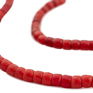 May include: A close-up of a red beaded necklace against a white backdrop. The necklace features small, square-shaped beads. The beads are a vibrant red colour, and the necklace is slightly curved.