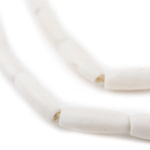 May include: A white beaded necklace made of smooth, cylindrical beads. The beads are strung together with a thin, white thread.