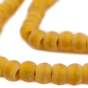 May include: A close-up of a strand of amber-colored beads. The beads are cylindrical with rounded edges and appear to be made of a translucent material. The beads are strung together, creating a necklace or bracelet.