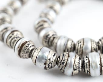 May include: A close-up of a silver and white beaded necklace. The beads are round and have a textured surface. The necklace is made of metal and has a silver finish.