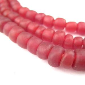 Pode incluir: Um fio de contas de vidro vermelho escuro. As contas são redondas e têm uma forma ligeiramente irregular. São enfiadas em um fio transparente.