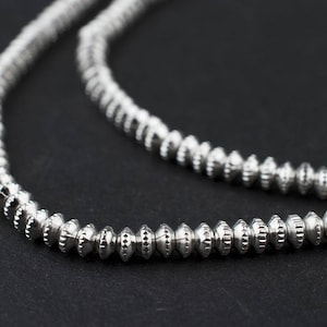 May include: A silver necklace with small, round beads that have a textured surface.