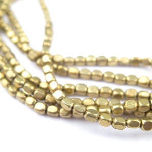 Puede incluir: Una hebra de cuentas de metal de color dorado, cada cuenta tiene forma cuadrada con bordes redondeados. Las cuentas están enhebradas en una cadena larga.