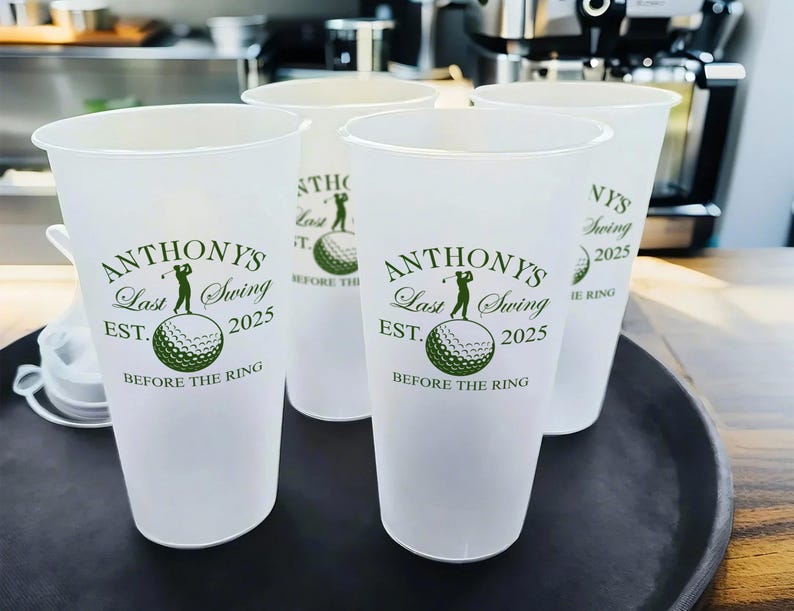 May include: Four white plastic cups with a golf-themed design. The cups have the text "Anthony's Last Swing Est. 2025 Before The Ring" printed on them.