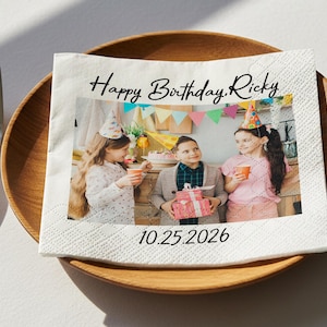Può includere: Un tovagliolo di carta bianco con la scritta "Happy Birthday Ricky" e la data "10.25.2026". Il tovagliolo presenta una foto di tre bambini a una festa di compleanno, con cappelli da festa e che tengono dei regali. Il tovagliolo è su un piatto di legno.