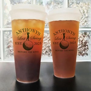 May include: Two clear plastic tumblers with brown liquid. Both tumblers have a black and gold design with the text "ANTHONY'S Last Swing EST. 2025 BEFORE THE RING".