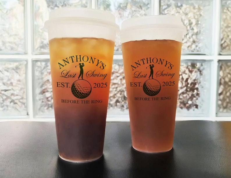 May include: Two clear plastic tumblers with brown liquid. Both tumblers have a black and gold design with the text "ANTHONY'S Last Swing EST. 2025 BEFORE THE RING".