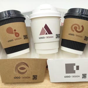 Puede incluir: Tres tazas de café desechables con tapas negras y mangas marrones, y una taza blanca con tapa blanca. Las mangas y las tazas tienen logotipos y el texto "LOGO / DESIGN". También se muestran dos mangas adicionales.