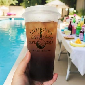 May include: A clear plastic cup with a black lid and a black and white graphic that says "Anthony's Last Swing Est. 2025 Before The Ring". The graphic features a golfer hitting a golf ball.