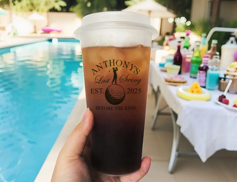 May include: A clear plastic cup with a black lid and a black and white graphic that says "Anthony's Last Swing Est. 2025 Before The Ring". The graphic features a golfer hitting a golf ball.