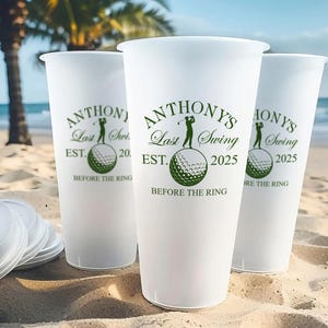 May include: Three white plastic cups with green text and a golf ball graphic. The text on the cups reads "Anthony's Last Swing Est. 2025 Before the Ring".