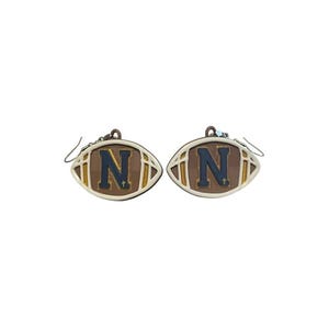 May include: A pair of earrings shaped like footballs. Each earring is brown with a tan border and a navy blue letter "N" in the center. The earrings have silver-colored hooks.
