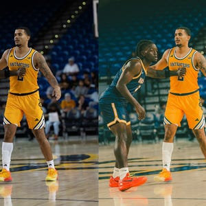 May include: Two basketball players on a court, one wearing a yellow jersey with "ANT EATERS" written on it, the other wearing a blue jersey. Both players are wearing basketball shorts and sneakers.