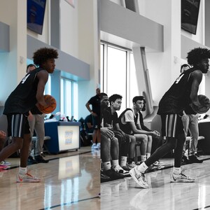 May include: A young man wearing a black and white basketball jersey dribbles a basketball while standing in a gym. Other young men are sitting on a bench in the background.