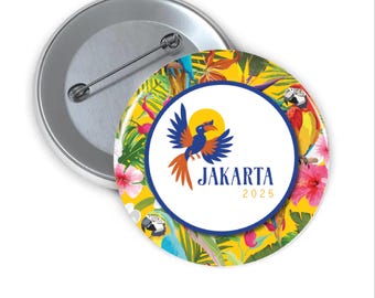 Puede incluir: Una chapa redonda con un alfiler plateado. El diseño presenta un fondo amarillo con hojas tropicales y loros. Un círculo blanco central muestra un logotipo de pájaro azul y naranja y el texto "JAKARTA 2025".
